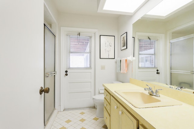 bathroom with a shower with door, vanity, toilet, and a skylight