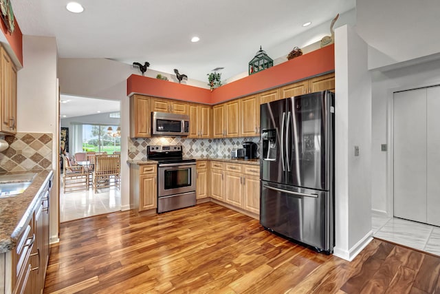 kitchen featuring light stone countertops, lofted ceiling, appliances with stainless steel finishes, and light wood-type flooring