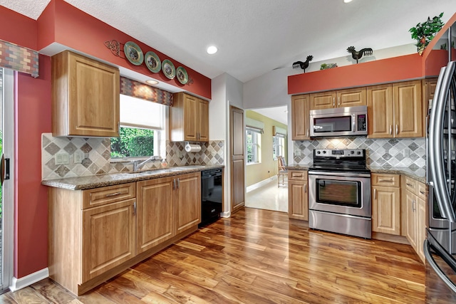 kitchen featuring backsplash, light stone countertops, wood-type flooring, sink, and stainless steel appliances