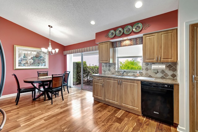 kitchen with black dishwasher, hanging light fixtures, light stone countertops, vaulted ceiling, and light wood-type flooring