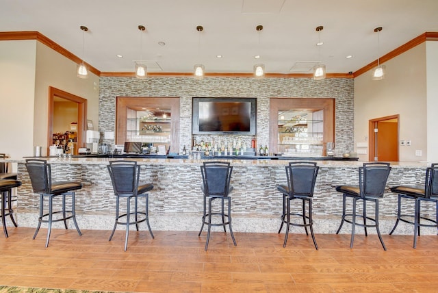 bar featuring ornamental molding, hanging light fixtures, and light wood-type flooring