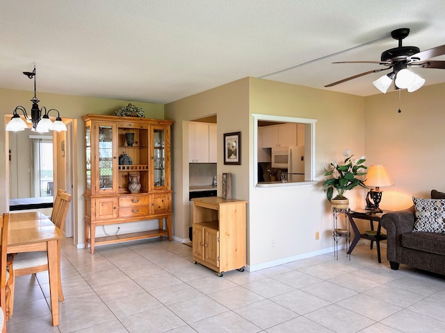 kitchen featuring hanging light fixtures, light tile patterned floors, white cabinets, white fridge, and ceiling fan with notable chandelier