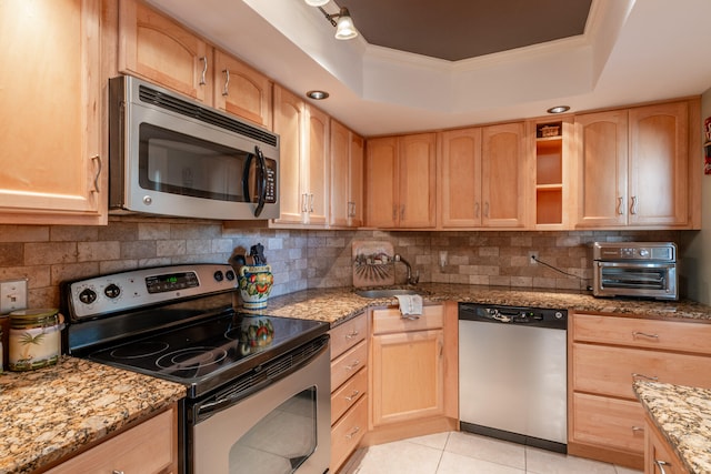 kitchen featuring light brown cabinets, light tile patterned floors, light stone countertops, appliances with stainless steel finishes, and a tray ceiling