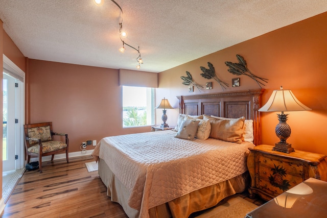 bedroom featuring light hardwood / wood-style flooring, rail lighting, and a textured ceiling