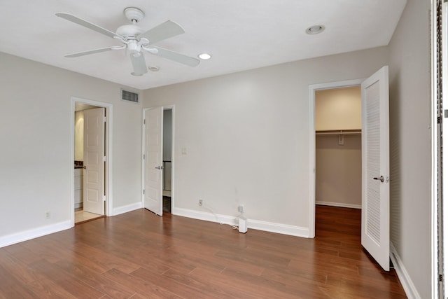 unfurnished bedroom featuring a spacious closet, ceiling fan, dark wood-type flooring, and a closet