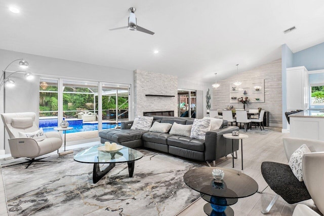 living room featuring vaulted ceiling, a fireplace, light wood-type flooring, and a healthy amount of sunlight