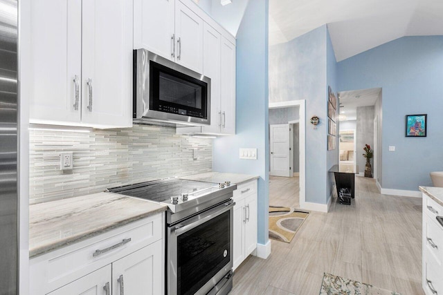 kitchen featuring lofted ceiling, light stone counters, backsplash, white cabinetry, and stainless steel appliances