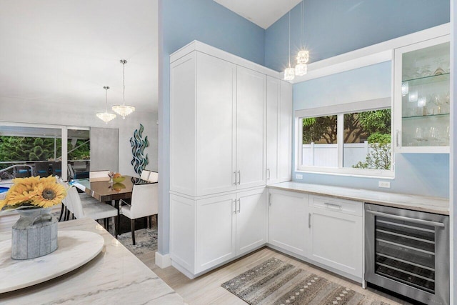 interior space with wine cooler, white cabinets, hanging light fixtures, and light stone countertops