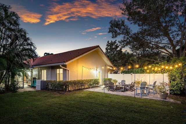 back house at dusk featuring a patio, a yard, and central air condition unit