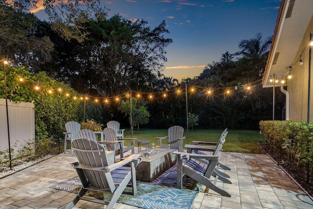 patio terrace at dusk featuring an outdoor fire pit and a lawn