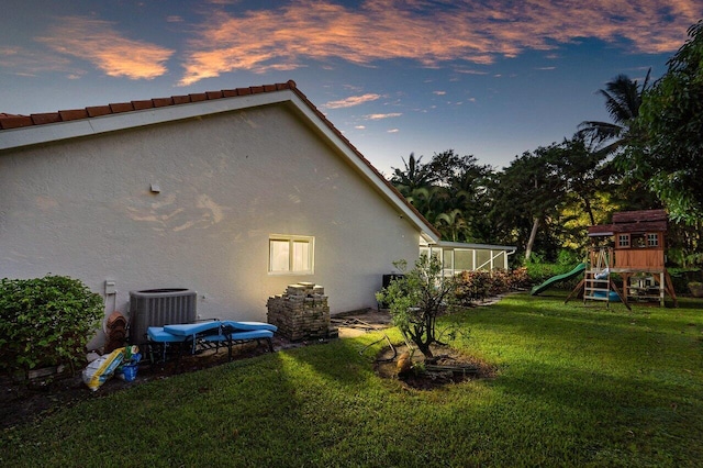 property exterior at dusk featuring central air condition unit, a lawn, and a playground