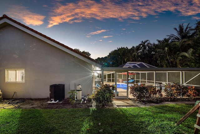 back house at dusk with a patio area, a lanai, and a lawn