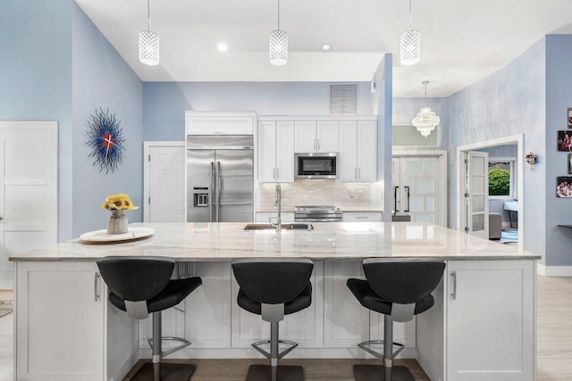 kitchen with light stone counters, appliances with stainless steel finishes, a spacious island, white cabinetry, and sink