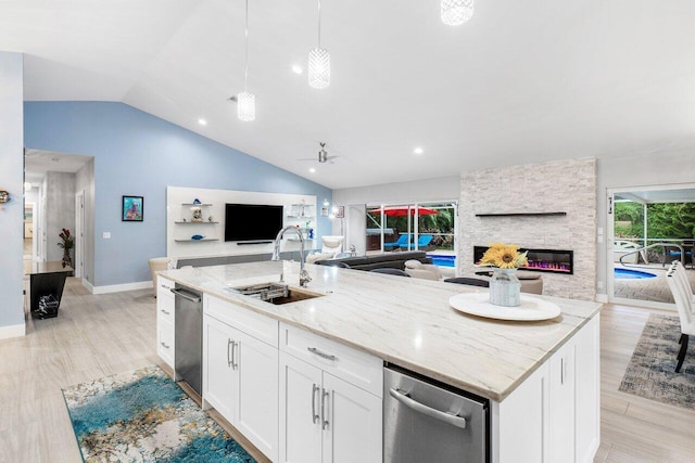 kitchen featuring lofted ceiling, light hardwood / wood-style flooring, an island with sink, white cabinetry, and a fireplace