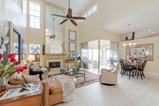 living room with a towering ceiling, light hardwood / wood-style flooring, ceiling fan with notable chandelier, and plenty of natural light