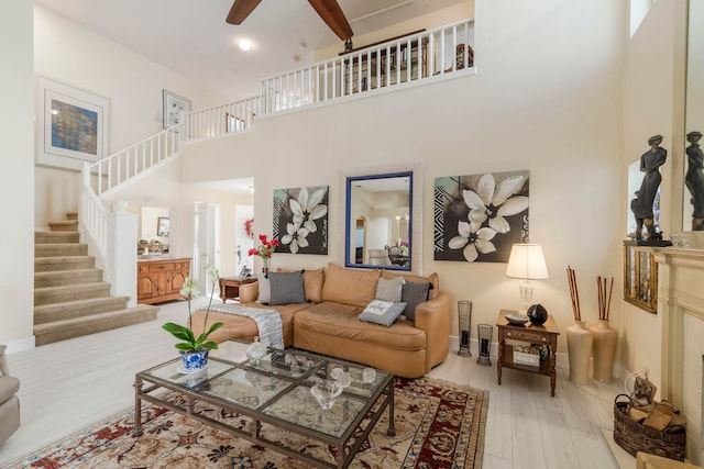 living room with ceiling fan, a towering ceiling, light hardwood / wood-style flooring, and beamed ceiling