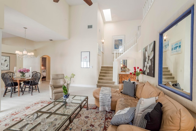 carpeted living room with ceiling fan with notable chandelier, high vaulted ceiling, and a skylight