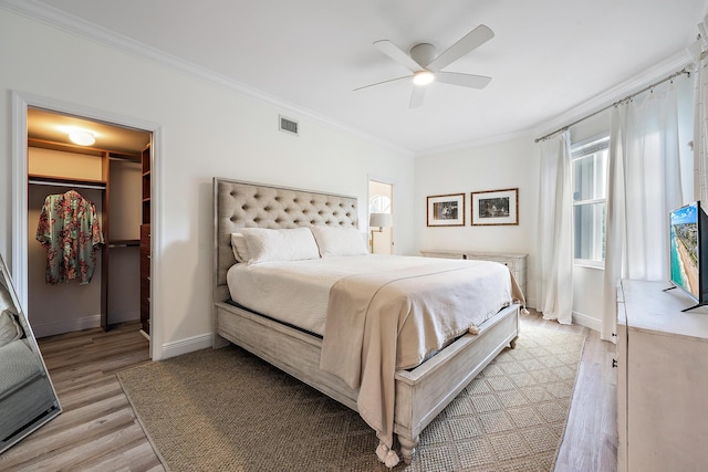 bedroom with a walk in closet, ceiling fan, ornamental molding, light hardwood / wood-style floors, and a closet