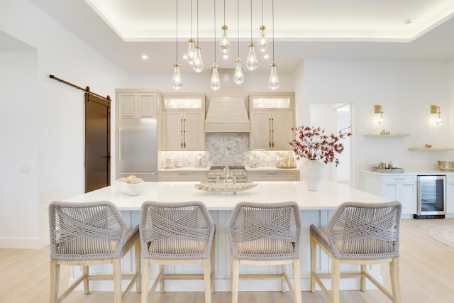 kitchen with light hardwood / wood-style floors, beverage cooler, a spacious island, built in refrigerator, and a barn door