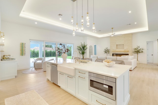 kitchen with stainless steel appliances, a center island with sink, a raised ceiling, and sink