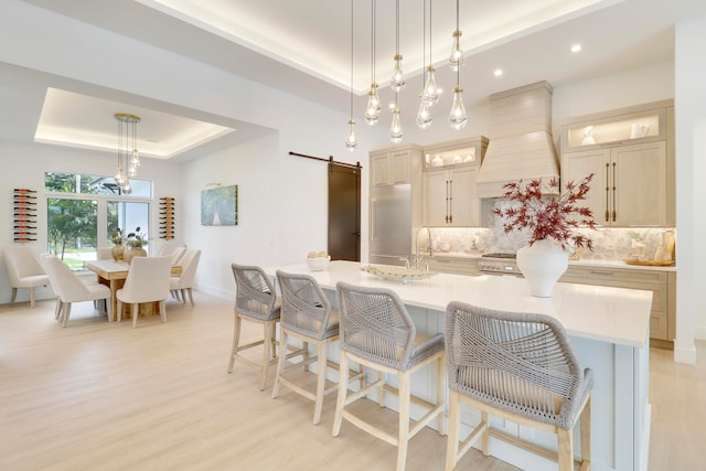 kitchen featuring a barn door, a large island with sink, custom range hood, and a raised ceiling