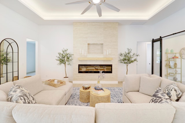 living room with a barn door, ceiling fan, a fireplace, and a tray ceiling