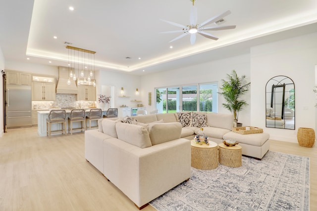 living room with ceiling fan, light wood-type flooring, and a tray ceiling