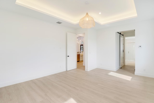 empty room featuring light wood-type flooring, a tray ceiling, and a barn door