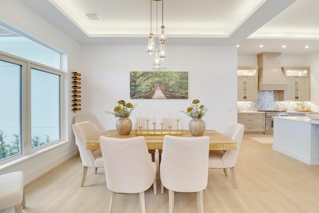 dining room featuring a wealth of natural light, a raised ceiling, and light hardwood / wood-style flooring