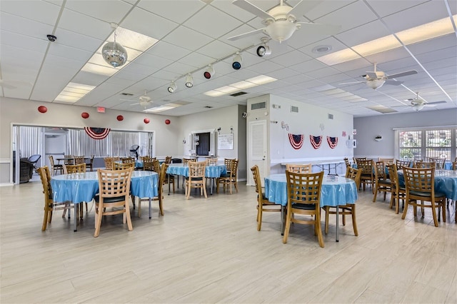 dining area with a paneled ceiling, ceiling fan, and light hardwood / wood-style flooring