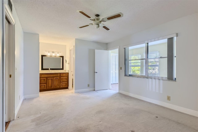 unfurnished bedroom featuring light colored carpet, ensuite bath, and a textured ceiling