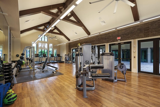 exercise room featuring hardwood / wood-style flooring, ceiling fan, brick wall, and high vaulted ceiling