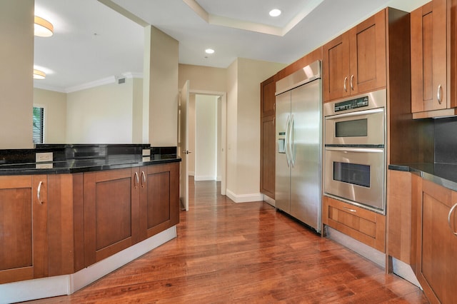 kitchen with dark hardwood / wood-style floors, dark stone countertops, ornamental molding, and stainless steel appliances