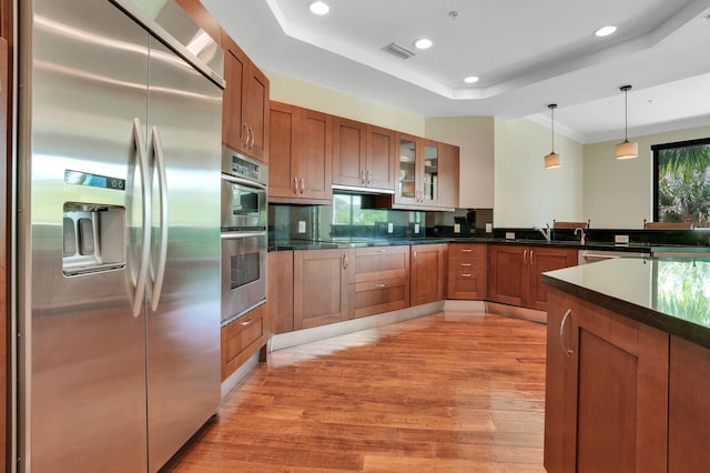 kitchen with decorative light fixtures, stainless steel appliances, a tray ceiling, and light hardwood / wood-style floors