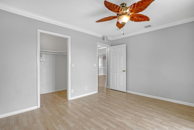 unfurnished bedroom with ceiling fan, a walk in closet, a closet, light wood-type flooring, and crown molding