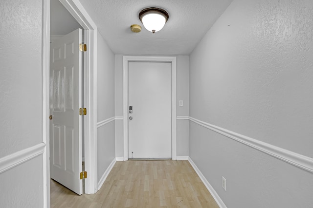 hallway with a textured ceiling and light hardwood / wood-style flooring