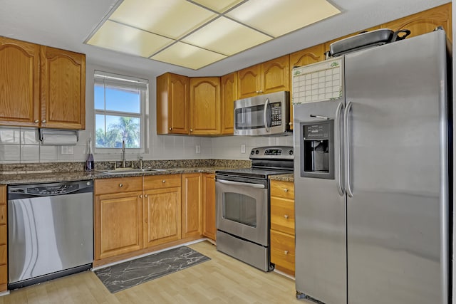 kitchen with sink, backsplash, dark stone counters, stainless steel appliances, and light wood-type flooring