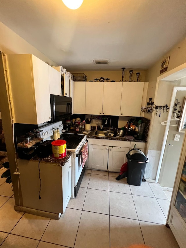 kitchen with white electric range oven, sink, light tile patterned floors, and white cabinetry