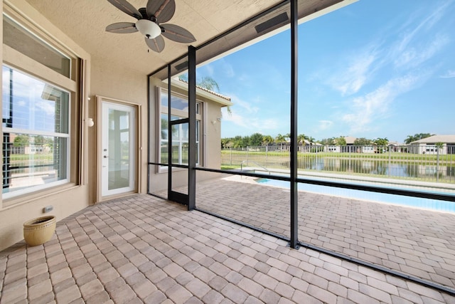 unfurnished sunroom with ceiling fan and a water view