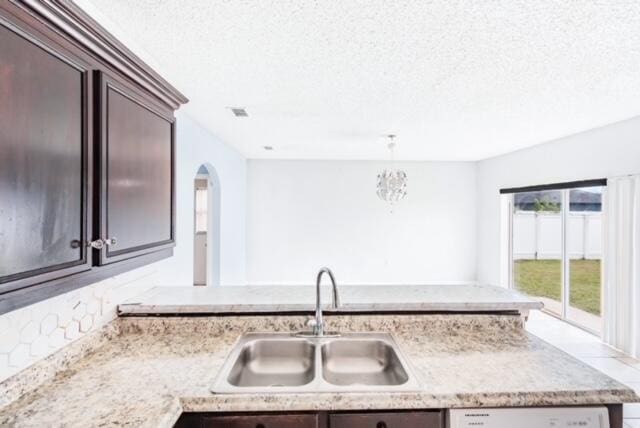 kitchen featuring sink, white dishwasher, a textured ceiling, dark brown cabinets, and pendant lighting