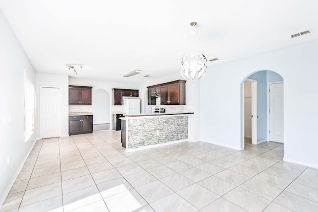 kitchen featuring a notable chandelier, dark brown cabinets, white refrigerator, and decorative backsplash