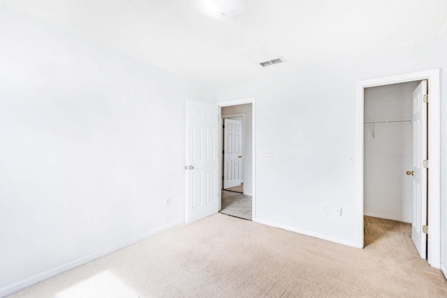 unfurnished bedroom featuring a closet, a spacious closet, and light colored carpet