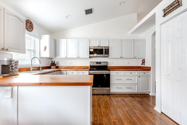 kitchen featuring appliances with stainless steel finishes, lofted ceiling, kitchen peninsula, and white cabinets