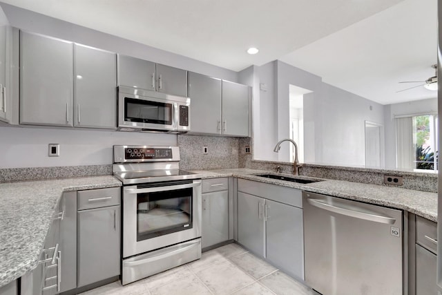 kitchen featuring sink, ceiling fan, stainless steel appliances, gray cabinets, and light stone counters