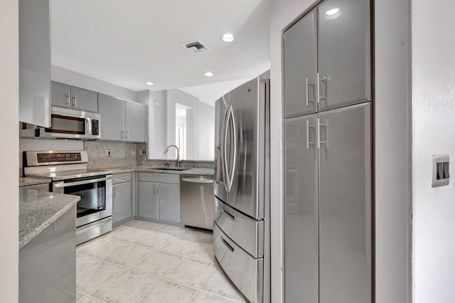 kitchen featuring light stone countertops, sink, light tile patterned flooring, stainless steel appliances, and gray cabinets