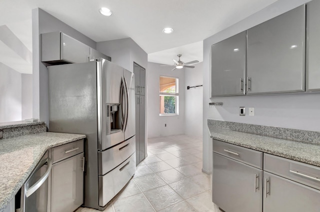 kitchen with gray cabinetry, stainless steel appliances, a barn door, light stone counters, and ceiling fan