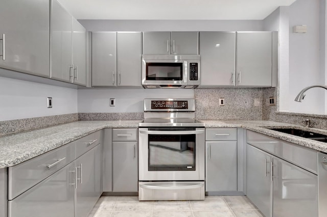 kitchen with light stone countertops, appliances with stainless steel finishes, gray cabinetry, and light tile patterned floors