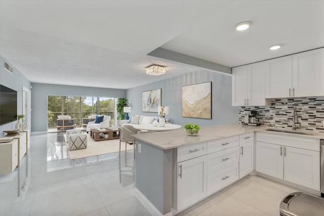 kitchen with kitchen peninsula, light stone countertops, sink, and white cabinets