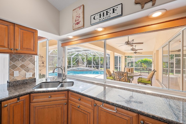 kitchen with backsplash, ceiling fan, dark stone countertops, and sink