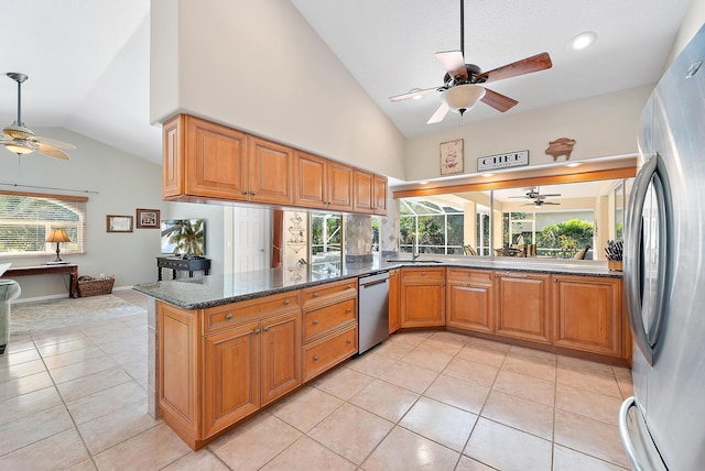 kitchen with kitchen peninsula, appliances with stainless steel finishes, light tile patterned floors, and dark stone countertops